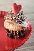 A romantic cupcake decorated with coloured sprinkles and a heart