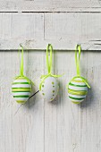 Three painted eggs hanging on white wooden wall