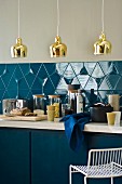 Küchenzeile mit blauen Unterschränken, Küchenutensilien vor blau gefliestem Spritzschutz & Messing-Hängeleuchten