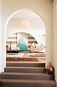 Carpeted steps leading through arched doorway and view into living area with ethnic rugs and modern furnitire