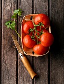 Tomatoes in a wooden basket with parsley and a knife