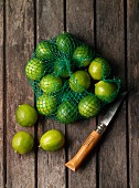 Limes in a net with a knife on a wooden surface