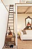 Vintage-Holzleiter führt auf weiß gestrichene Holz-Galerie, darunter ecru-farbene Polstercouch mit antikem verziertem Spiegel an der Wand