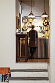 Raised, vintage kitchen with pans hung on wall and young woman standing at kitchen counter with striped curtain on base units