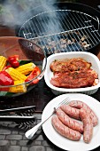 Marinated pork steaks, sausages and vegetables in front of a hot barbecue