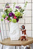 Sommerblumenstrauß in weißer Retro-Porzellanvase auf Holzstuhl mit karibischer Mädchenfigur arrangiert