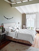 Double bed at comfortable height with upholstered headboard against taupe wall in elegant bedroom with rustic charm