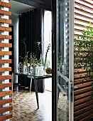 View through terrace doors into interior; various glass vases and plant stems on table