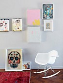 White, Charles Eames rocking chair below various pictures on wall; framed modern picture of skull on floor
