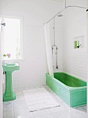 Green vintage pedestal sink and vintage bathtub with shower curtain in white-tiles bathroom with marble floor