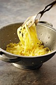 Linguine in a colander with pasta tongs