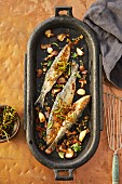 Roast sardines with vegetables and herbs in an iron pan (seen from above)