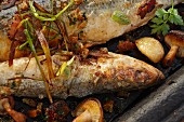 Roasted sardines with vegetables and herbs in an iron pan (close-up)