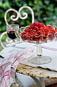 Glass dish of fresh redcurrants and raspberries on vintage metal table in garden
