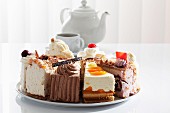 Various different slices of cake on a plate with a teapot and a cup in the background