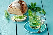 A glass of mint tea next to a loaf of bread with cream cheese and chives