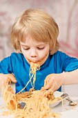 A little boy eating spaghetti with his fingers