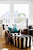 Armchair and pouffe in wide, black and white stripes in front of living room window