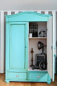 Pastelltürkis gestrichener Vintage Schrank mit Patina, Blick durch die offene Tür auf Deko Objekte
