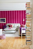 Wandbord mit Bücherstapeln; dahinter Wohnzimmer mit rot-pink gestreifter Tapete