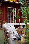 Scatter cushions and basket on wooden bench painted pale grey in front of simple wooden cabin