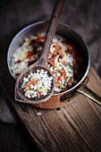 Risotto rice with a spice mixture made from dried tomatoes, herbs and garlic in a copper pot and on a wooden spoons