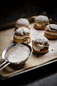 Semlor (Swedish cakes) on a baking tray next to a sieve of icing sugar