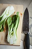 A hlaved bok choy on a wooden board with a knife