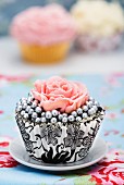 A cupcake decorated with silver pearls and a sugar rose