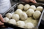 Koch hält Backblech mit ungebackenen Arancini