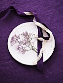 White plate on purple tablecloth decorated with purple flowers and satin and lace ribbons