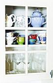 Teapots, cups and glasses in crockery cupboard with lattice door