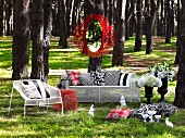 Mirror with red metal frame hanging on tree & white, wire mesh outdoor furniture with scatter cushions in woodland clearing
