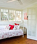 Country-style bedroom with white metal bed & floral bedspread in front of ribbon window