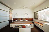 Half-height shelving in front of double bed flanked by bedside lamps in modern bedroom with glass sliding elements