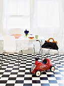 A red children's car with an eating area in the background on a black and white checked floor
