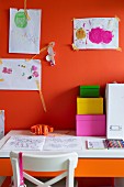 Colourful cardboard storage boxes on desk below child's drawings on orange wall