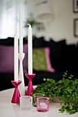 Set of pink and white candlesticks and tealight holders next to bowl of leafy twigs