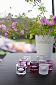 Lila Gartenstrauss in weisser Vase und Windlichter auf Tisch mit schwarzem Tischtuch