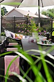 Tisch mit Tassen, Windlichtern und Gartenstrauss unter Sonnenschirm auf der Terrasse, im Hintergrund Hängematte