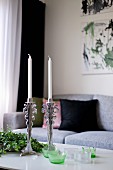 Silber Kerzenständer mit weissen Kerzen und Windlichter auf Couchtisch vor hellgrauem Sofa