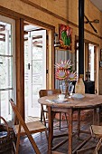 Old wooden furniture and vase of protea in dining area in house with many reclaimed elements