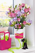 Bouquet of purple freesias and eustomas in vase wrapped in colourful woollen yarn
