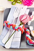 Cutlery, linen napkin and flower wrapped in napkin ring made from plaited woollen yarn