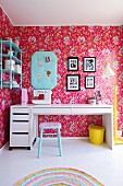 Moderner, weisser Schreibtisch in nostalgischem Kinderzimmer, an Wand Tapete mit Blumenmuster auf pinkfarbenem Hintergrund