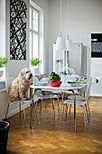 Dog sitting on white shell chair with metal frame at set table in modern dining room with traditional atmosphere