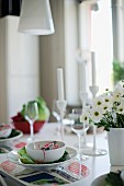 Place setting with white bowl on table mat and vase of flowers to one side