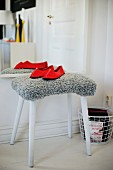 Red slippers on stool with grey, fur-like cover in front of mirror on wall