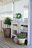 Potted herbs and lantern on wooden floor in front of white side tables on veranda