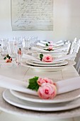 weiße Gedecke mit Rosenblüten und Stoffserviette auf weißem Holztisch